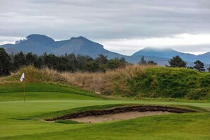 A golf course with a flag, bunkers, and a mountain backdrop.
