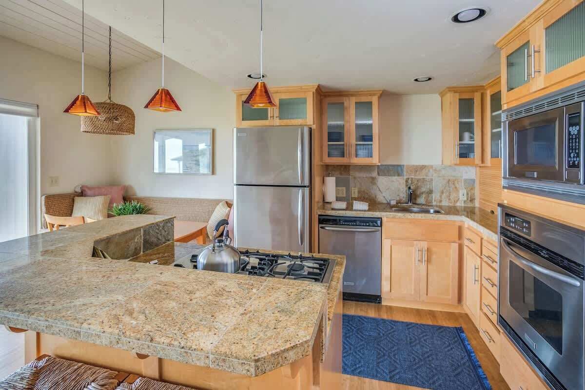 A kitchen with granite countertops, stainless steel appliances, wooden cabinets, and pendant lighting.