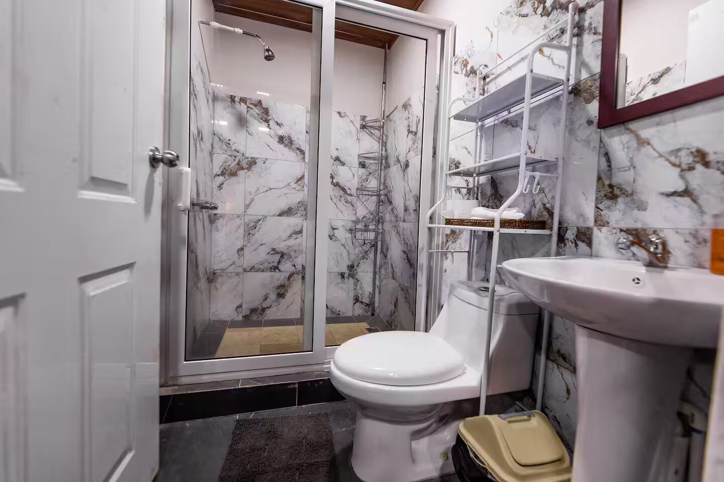 A bathroom with a shower, toilet, and sink, all with marble-like tiles.