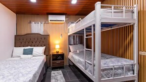 A room with bunk beds, a bedside table with a lamp, an air conditioning unit, and a window with curtains.