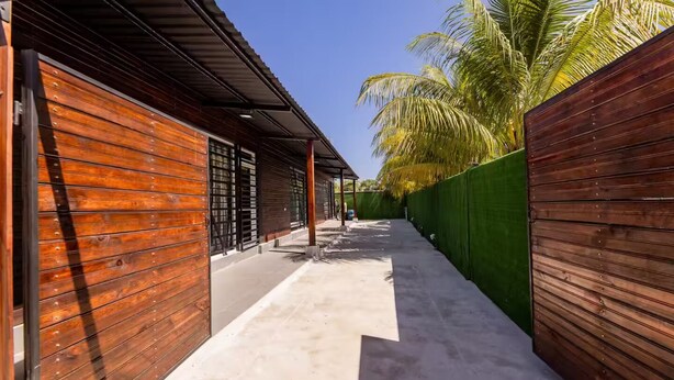 A narrow pathway flanked by wooden walls and a green fence, leading to a building with a metal roof.
