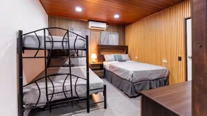A room with bunk beds, a single bed, a wooden ceiling, an air conditioner, and a bedside table.