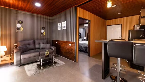 A modern living room with a sofa, a coffee table, and a kitchen area with a bar stool.