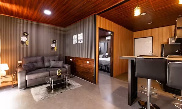 A modern living room with a sofa, a coffee table, and a kitchen area with a bar stool.