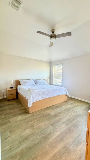 Ein Schlafzimmer mit einem Bett, einem Nachttisch, einem Deckenventilator und einem Fenster mit Jalousien.