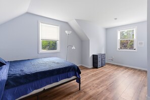 Une chambre à coucher avec un lit, deux fenêtres, une lampe sur pied et une commode.