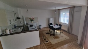 Una cocina compacta con refrigerador, estufa y lavamanos. Hay un comedor con mesa y sillas. Un ventanal proporciona luz natural.