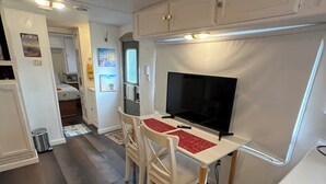 Ein kompaktes Wohnmobil-Interieur mit einer Küchenzeile, einem Essbereich mit Tisch und Stühlen sowie einem Fernseher.