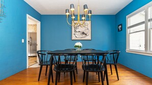 Uma sala de jantar com uma mesa redonda, seis cadeiras, um candelabro e uma obra de arte emoldurada na parede.