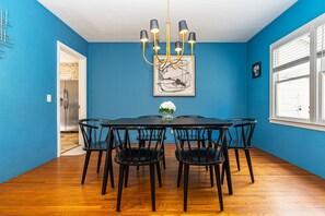 Un comedor con una mesa redonda, seis sillas, una araña y una obra de arte enmarcada en la pared.