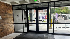 Entrada de hotel con puerta de cristal, pared de madera y un felpudo estampado.