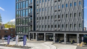 Un edificio moderno con fachada geométrica, un estacionamiento y un letrero que dice 'Now Leasing'.