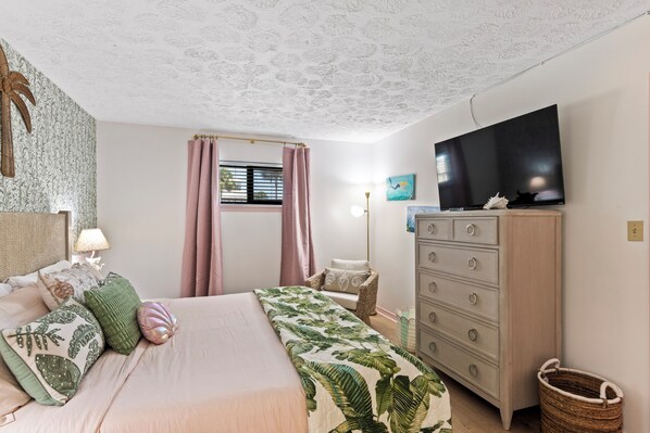 Un dormitorio con cama, cómoda, televisor y ventana con cortinas.