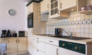 Eine kleine Küche mit weißen Schränken, einer Mikrowelle, einer Kaffeemaschine, einem Wasserkocher und einem Spülbecken.
