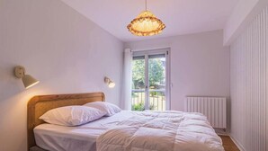 Ein Schlafzimmer mit Bett, einer Hängelampe, einer Wandleuchte, einem Fenster mit Aussicht und einer Heizung.