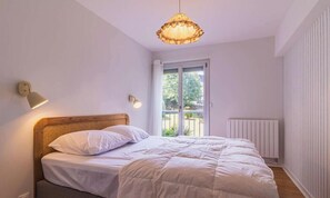 Ett sovrum med en säng, en hängande lampa, en vägglampa, ett fönster med utsikt och ett element.