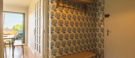 A room with a patterned wallpaper, a bench, a door, and a view of an outdoor area with a table and chairs.