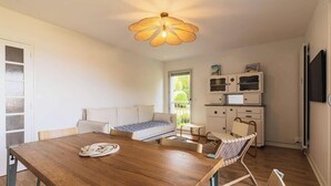 Ein modernes, helles Zimmer mit einem Holzesstisch, einer Couch, einem kleinen Fernseher und einem Schrank.