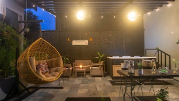 Un rincón acogedor al aire libre con una silla de mimbre, una mesa con cafetera y un letrero que dice 'BIENVENIDO'.