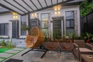 A modern outdoor seating area with wicker chairs and a hanging chair, surrounded by potted plants and a stone-tiled patio.