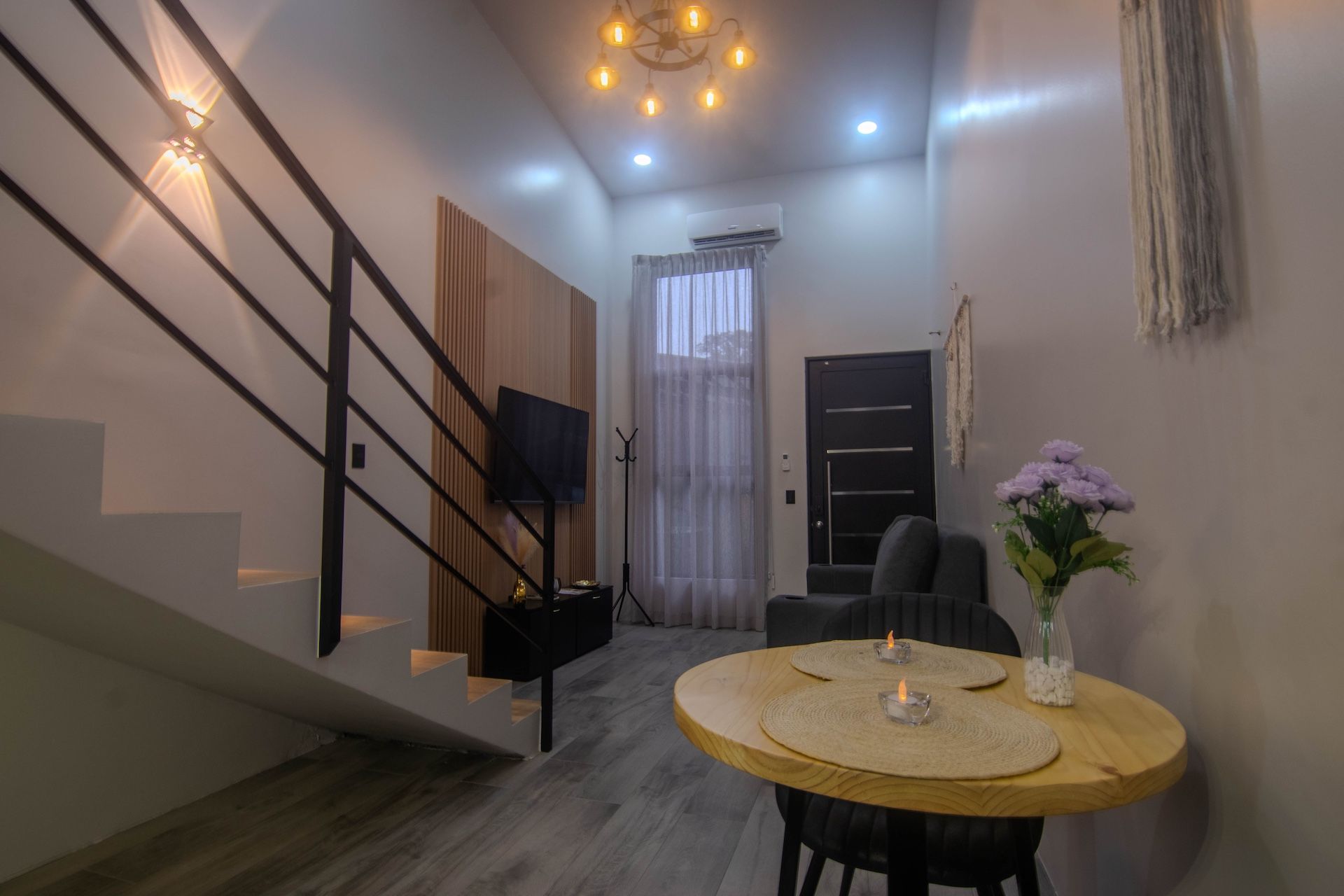Un espace de vie moderne comprenant un escalier, une table ronde en bois avec une bougie, et un téléviseur fixé au mur.