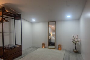 A minimalist room with a bed, a wooden bench, a large mirror, and a potted plant.