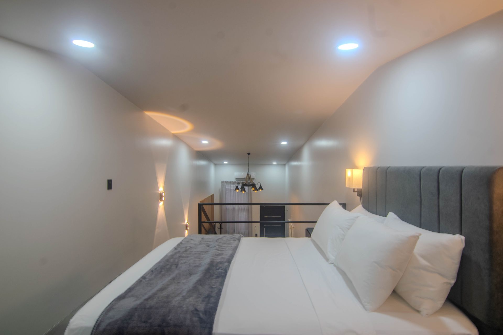 Un dormitorio moderno con una cama grande, cabecera gris e iluminación empotrada en el techo.