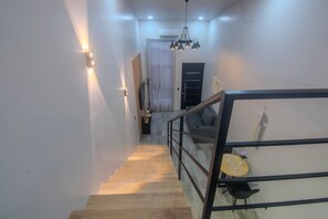 A staircase leading to a landing with a sofa and a small table, a black door, and a wall-mounted light fixture.