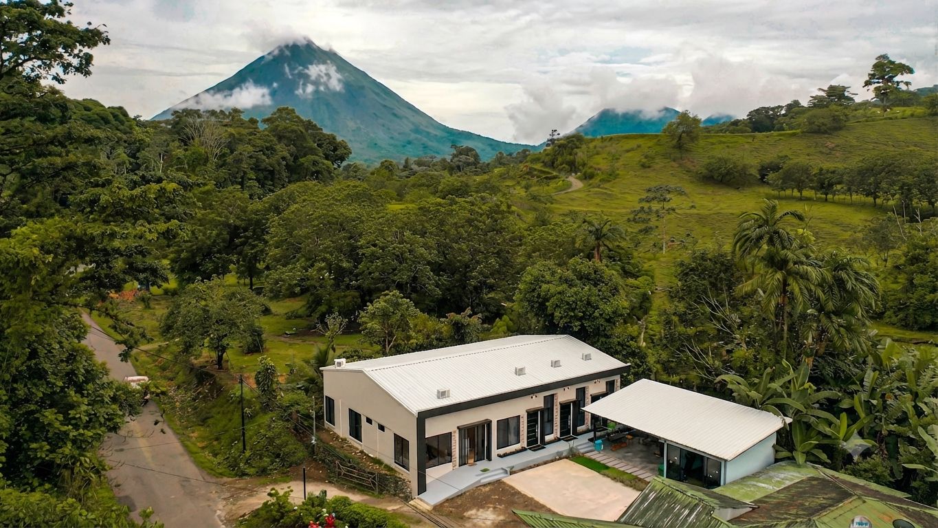Une maison moderne à deux étages, dotée d’un toit plat, entourée d’une végétation luxuriante et avec une montagne en toile de fond.