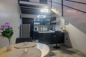 Una cocina moderna con microondas, cafetera y lavabo. Hay un comedor con mesa y sillas, y un jarrón con flores.