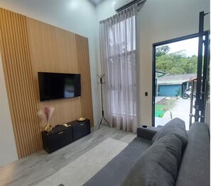 Un salon moderne avec un téléviseur à écran plat fixé sur un mur recouvert de panneaux en bois, un meuble de rangement noir, un trépied et un canapé gris.