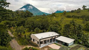 A modern two-story house with a flat roof, surrounded by lush greenery and a mountain in the background. - New! Luna Negra Luxury Suites & Spa. Your romantic getaway in Arenal (El Castillo)