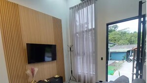 Una sala de estar moderna con un televisor de pantalla plana montado en una pared de paneles de madera, un mueble de entretenimiento negro, un trípode y un sofá gris.