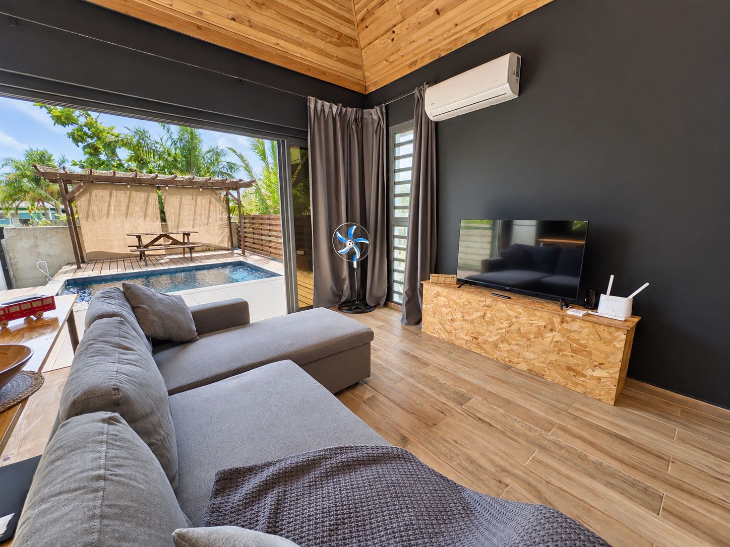 Un salon moderne avec une piscine, un canapé, un téléviseur et un comptoir d’accueil en bois.