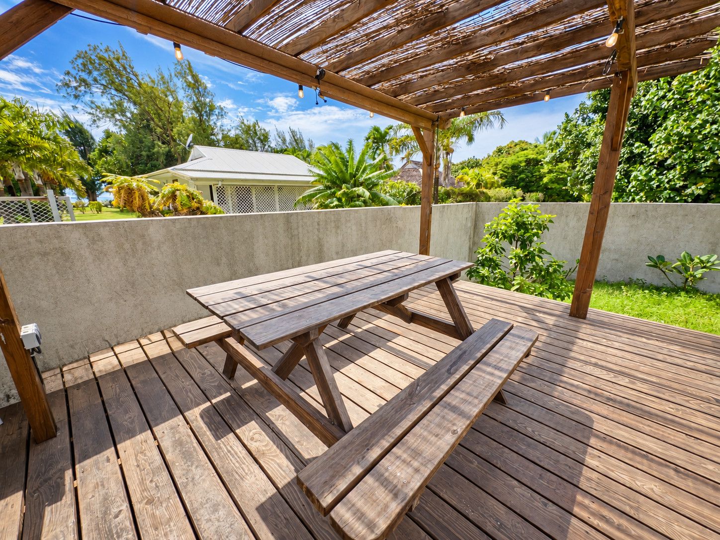 Une terrasse en bois avec une table de pique-nique, entourée d’une végétation luxuriante et sous un ciel dégagé.