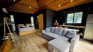 A modern living space with a wooden ceiling, a sofa, a bed, and a kitchen area.