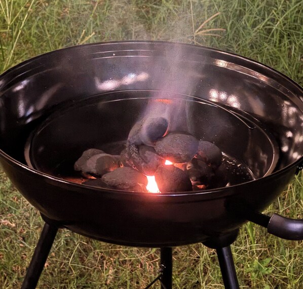 Ein schwarzer Metallgrill mit Holzkohle auf einem Gestell im Freien.