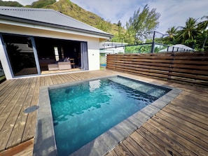 En swimmingpool med en træterrasse, et overdækket siddeområde og udsigt til en skråning.