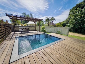 Et rektangulært swimmingpool med en træterrasse, en pergola og et picnicbord.