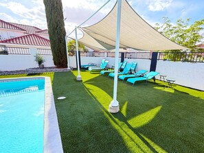 Ein Poolbereich mit Kunstgrasanlage, Liegestühlen und einem Sonnensegel.