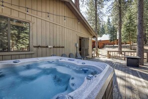 Eine Holzhütte mit Whirlpool, Terrasse und Sitzgelegenheit im Freien, umgeben von Bäumen.