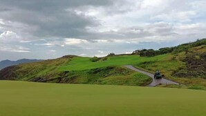 A golf course with a winding road and a vehicle on the path.