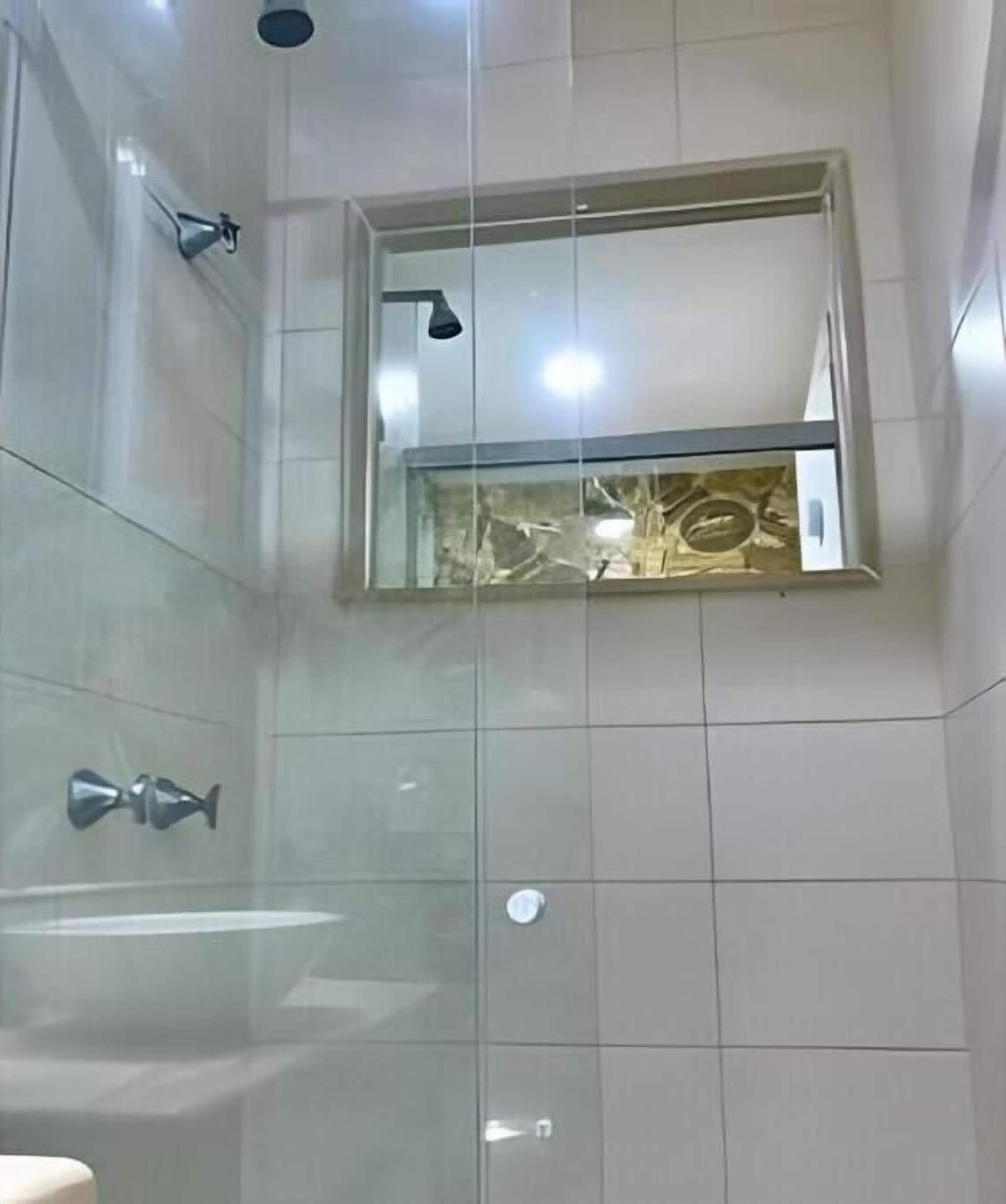 A bathroom with a shower, a mirror, and a window.