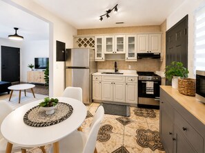 A modern kitchen with white cabinets, a stainless steel refrigerator, a stove, and a dining area with a white table and chairs. - Cozy 2BR Retreat w/Private Patio Near Downtown, Airport & Hospitals (Miami)