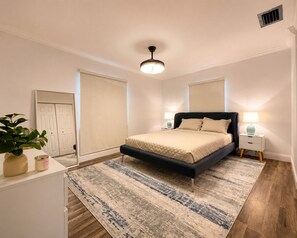 Un dormitorio con cama, mesitas de noche, una planta en maceta y una ventana con persianas.