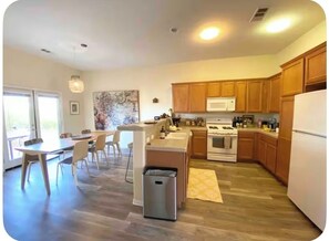 A modern kitchen with wooden cabinets, a central island, and a dining area with chairs. - The Dreamcatcher with Game Room, Jacuzzi, pooltable, cowboy jacuzzi and foosball (Joshua Tree)