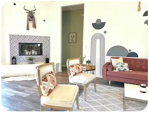 A living room with a fireplace, a sofa, two armchairs, and a patterned rug. - The Dreamcatcher with Game Room, Jacuzzi, pooltable, cowboy jacuzzi and foosball (Joshua Tree)