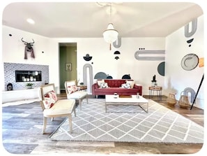 A modern living room with a fireplace, a red sofa, a white coffee table, and a geometric rug. - The Dreamcatcher with Game Room, Jacuzzi, pooltable, cowboy jacuzzi and foosball (Joshua Tree)