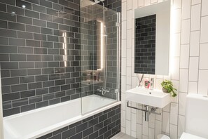 Ein modernes Badezimmer mit einer Duschkabine, einem weißen Waschbecken und einem Spiegel darüber.