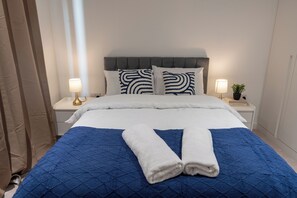 Ein ordentlich bezogenes Bett mit einer blauen Decke, weißen Kissen und zwei zusammengerollten Handtüchern.